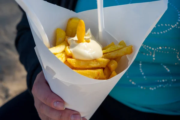 Eatiog of street or take away food fresh baked french fried potatoes chips in paper cone