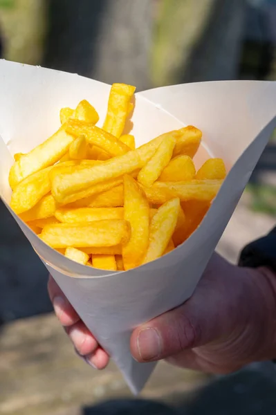 Eatiog of street or take away food fresh baked french fried potatoes chips in paper cone