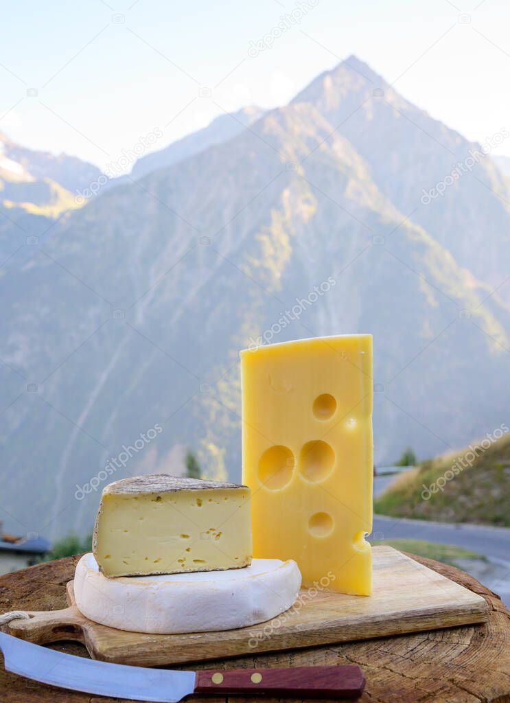 Cheese collection, French emmental, tomme and reblochon de savoie cheeses served outdoor in Savoy region, with Alpine mountains peaks in summer on background