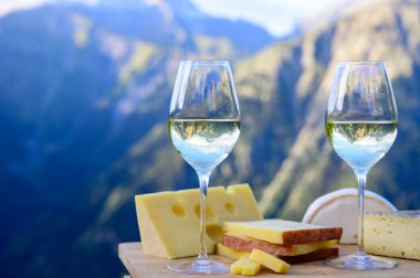Fransa 'nın Savoy bölgesinden lezzetli peynir ve şarap, Beaufort, abondance, emmental, tomme ve reblochon de savoie peynirleri ve yazın açık havada sunulan beyaz şarap arka planda Alp dağlarının zirveleri