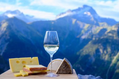 Fransa 'nın Savoy bölgesinden lezzetli peynir ve şarap, Beaufort, abondance, emmental, tomme ve reblochon de savoie peynirleri ve yazın açık havada sunulan beyaz şarap arka planda Alp dağlarının zirveleri
