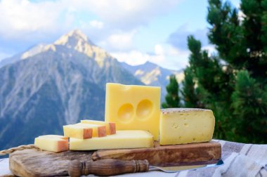 Peynir koleksiyonu, Fransız beaufort, abondance, emmental, tomme de savoie cheeses Savoy bölgesinde açık havada servis edilir, yaz aylarında Alp dağlarının zirveleri arka plandadır.