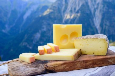 Peynir koleksiyonu, Fransız beaufort, abondance, emmental, tomme de savoie cheeses Savoy bölgesinde açık havada servis edilir, yaz aylarında Alp dağlarının zirveleri arka plandadır.