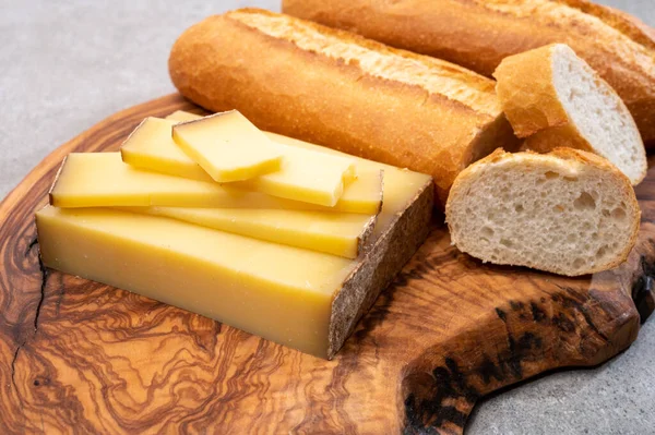 French food -  piece of cheese comte made from cow milk in region Franche-Comte in France and fresh baked baguette bread close up