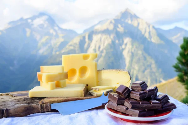 おいしいスイスチーズとダークピュアチョコレート グリュイエール アペンツェラーは背景に夏にアルパイン山のピークを屋外で提供しています — ストック写真