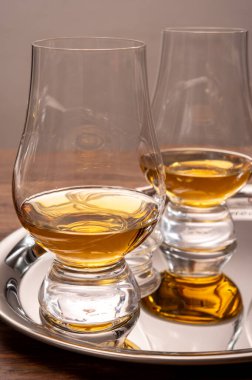 Çelik ayna tepsisinde sunulan viski bardakları yakından yansıtılıyor.