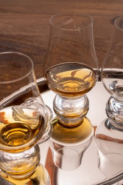 Çelik ayna tepsisinde sunulan viski bardakları yakından yansıtılıyor.