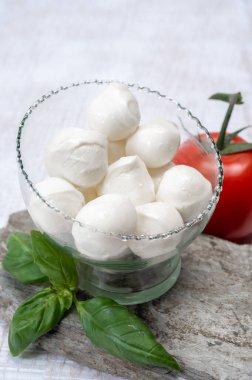 Kırmızı domates ve taze yeşil fesleğenle servis edilen taze, yumuşak mozzarella topları.