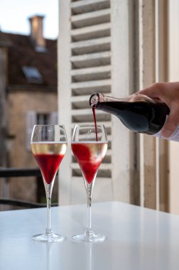 Kir Royal içen, Fransız aperatifi. Krema ve şampanyayla kaplanmış, genellikle flüt bardaklarıyla servis edilen, eski Fransız köyü manzaralı.