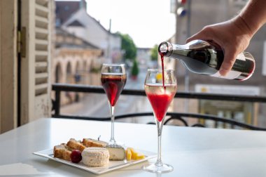 Kir Royal içen, Fransız aperatifi. Krema ve şampanyayla kaplanmış, genellikle flüt bardaklarıyla servis edilen, eski Fransız köyü manzaralı.