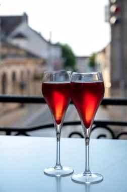 Kir Royal içen, Fransız aperatifi. Krema ve şampanyayla kaplanmış, genellikle flüt bardaklarıyla servis edilen, eski Fransız köyü manzaralı.