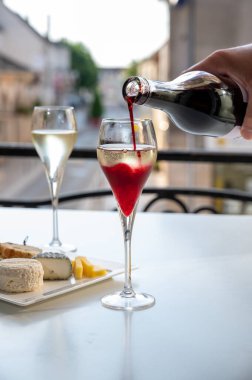 Kir Royal içen, Fransız aperatifi. Krema ve şampanyayla kaplanmış, genellikle flüt bardaklarıyla servis edilen, eski Fransız köyü manzaralı.