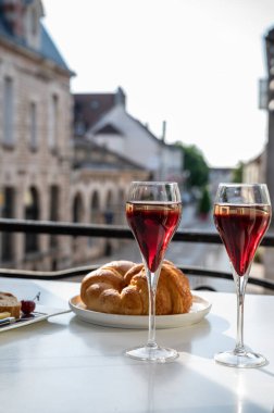 Kir Royal içen, Fransız aperatifi. Krema ve şampanyayla kaplanmış, genellikle flüt bardaklarıyla servis edilen, eski Fransız köyü manzaralı.