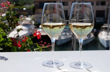 Fransız Riviera Cote d 'Azur' da yaz mevsiminde Cotes de Provence 'den gelen soğuk beyaz şarabı arka planda tekne ve yatlarla Port Grimaud, Var, Fransa' daki güneşli açık terasta içerken.