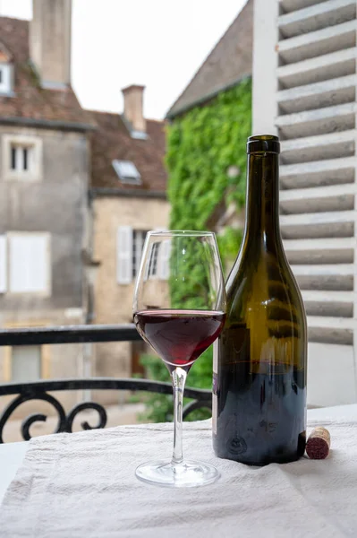 Tasting of burgundy red wine from grand cru pinot noir  vineyards, glass and bottle of red wine and view on old town street in Burgundy wine region, France