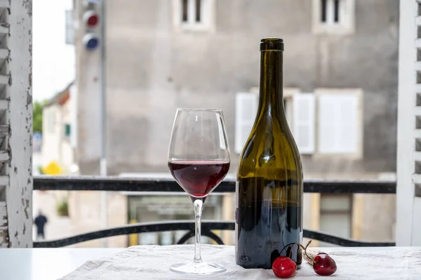 Tasting of burgundy red wine from grand cru pinot noir  vineyards, glass and bottle of red wine and view on old town street in Burgundy wine region, France