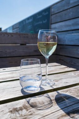 Güneşli bir günde deniz manzaralı terasta sunulan beyaz şarap ve maden suyu bardakları, yaz tatili.