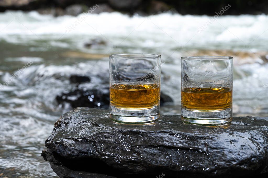 Glass of strong scotch single malt whisky with fast flowing mountain river on background, Scotland