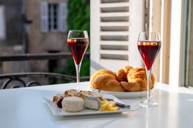 Kir Royal içen, Fransız aperatifi. Krema ve şampanyayla kaplanmış, genellikle flüt bardaklarıyla servis edilen, eski Fransız köyü manzaralı.