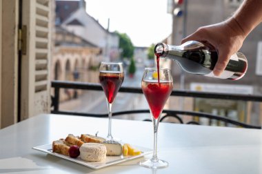 Kir Royal içen, Fransız aperatifi. Krema ve şampanyayla kaplanmış, genellikle flüt bardaklarıyla servis edilen, eski Fransız köyü manzaralı.
