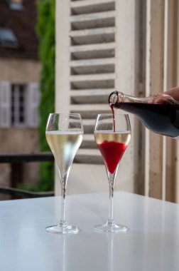 Kir Royal içen, Fransız aperatifi. Krema ve şampanyayla kaplanmış, genellikle flüt bardaklarıyla servis edilen, eski Fransız köyü manzaralı.