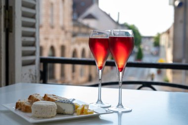 Kir Royal içen, Fransız aperatifi. Krema ve şampanyayla kaplanmış, genellikle flüt bardaklarıyla servis edilen, eski Fransız köyü manzaralı.