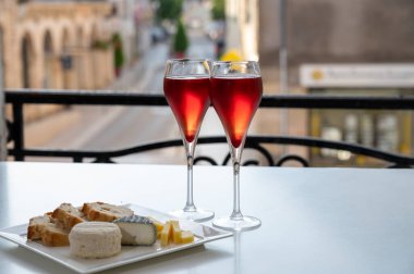 Kir Royal içen, Fransız aperatifi. Krema ve şampanyayla kaplanmış, genellikle flüt bardaklarıyla servis edilen, eski Fransız köyü manzaralı.