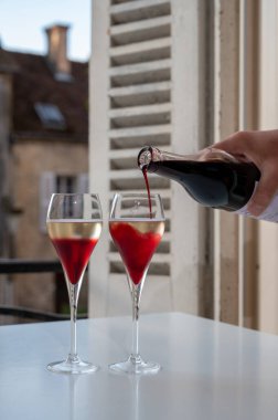 Kir Royal içen, Fransız aperatifi. Krema ve şampanyayla kaplanmış, genellikle flüt bardaklarıyla servis edilen, eski Fransız köyü manzaralı.