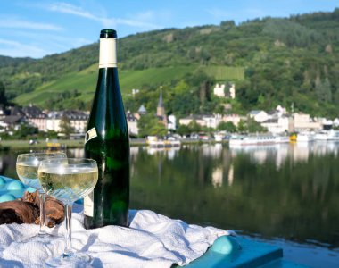 White quality riesling wine in green bottle served on old bridge across Mosel river with view on old German town in sunny day clipart