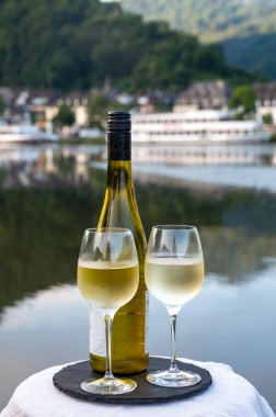 Mosel şarap bölgesinde beyaz kaliteli riesling şarabı tatmak için Mosel nehri ve Almanya 'nın güneşli günlerinde arka planda kalan eski Alman kasabası ile birlikte açık havada servis edilir.