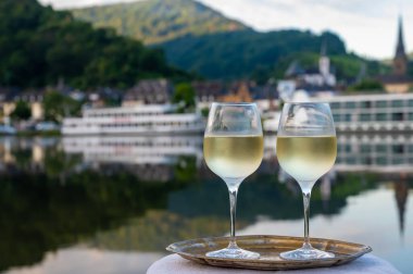 Tasting of white quality riesling wine served on outdoor terrace in Mosel wine region with Mosel river and old German town on background in sunny day, Germany clipart