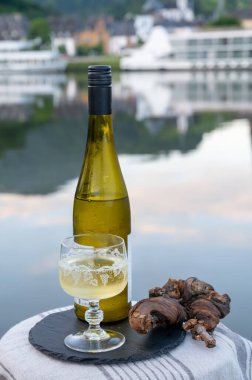 Mosel şarap bölgesinde beyaz kaliteli riesling şarabı tatmak için Mosel nehri ve Almanya 'nın güneşli günlerinde arka planda kalan eski Alman kasabası ile birlikte açık havada servis edilir.