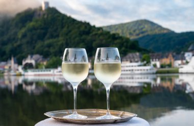Mosel şarap bölgesinde beyaz kaliteli riesling şarabı tatmak için Mosel nehri ve Almanya 'nın güneşli günlerinde arka planda kalan eski Alman kasabası ile birlikte açık havada servis edilir.