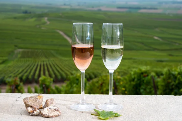 Glasses of white and rose brut champagne wine, firestones from vineyard soil and view on grand cru vineyards of Montagne de Reims near Verzenay, Champagne, France