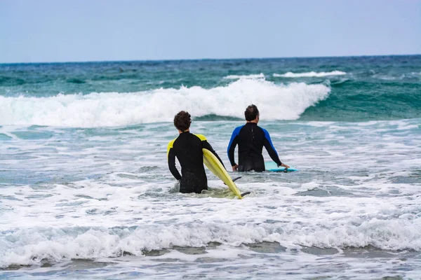 Unidentified surfers train in cold water of Atlantic ocean on famous surf Famara beach, Lanzarote, Canary islands, Spain