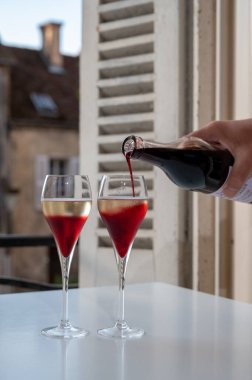 Kir Royal içen, Fransız aperatifi. Krema ve şampanyayla kaplanmış, genellikle flüt bardaklarıyla servis edilen, eski Fransız köyü manzaralı.