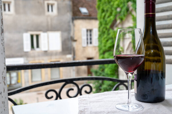 Дегустация бордового красного вина с виноградников Grand Cru pinot noir, бокал и бутылка красного вина и вид на старую улицу города в винном регионе Бургундии, Франция