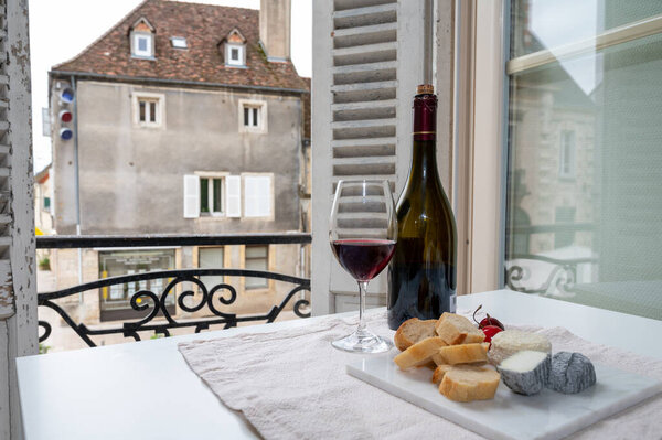 Дегустация бордового красного вина из виноградников Grand Cru pinot noir с французскими козьими сырами и видом на старую улицу города в винодельческом регионе Бургундия-Кот-де-Нуит, Франция