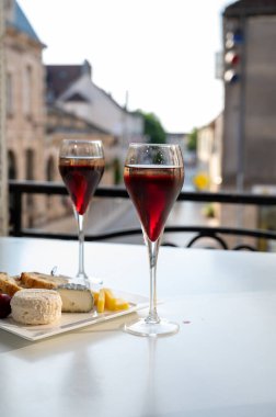Kir Royal içen, Fransız aperatifi. Krema ve şampanyayla kaplanmış, genellikle flüt bardaklarıyla servis edilen, eski Fransız köyü manzaralı.