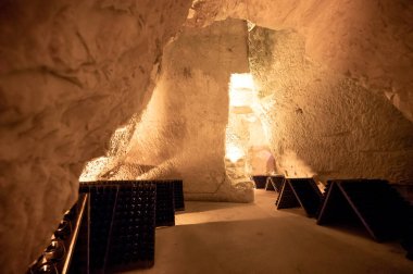 Derin ve uzun yeraltı mağaralarındaki raflarda şişeler şarap ve üzüm şarabından şampanya yapıyor Reims, Champagne, France 'ta.