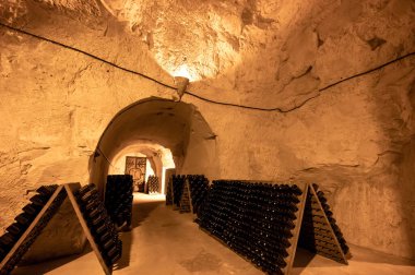 Derin ve uzun yeraltı mağaralarındaki raflarda şişeler şarap ve üzüm şarabından şampanya yapıyor Reims, Champagne, France 'ta.