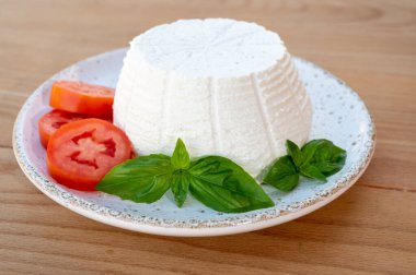 Peynir koleksiyonu, beyaz İtalyan yumuşak peyniri ricotta. Taze domates ve fesleğenle servis ediliyor. Arka planda İtalyan evleri var.