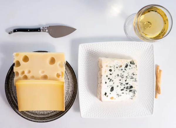 Cheese collection, hard French cheese comte made from cow milk with rind in Franche-Comte region, blue cheese roquefort and emmentaler cheese, France, served with white wine close up