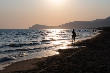 Güneş ışığında gün batımında yüzen insanların siluetleri, Sperlonga yakınlarındaki kumlu plajlar, Lazio, İtalya, yaz tatili
