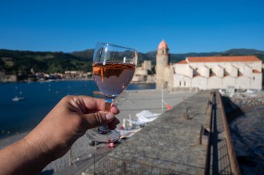 Güneş ışığında bir bardak gül Collioure AOC şarabı, Collioure kasabası manzaralı, renkli evler, kilise, kale ve plajlar, Occitanie, Fransa, turist beldesi