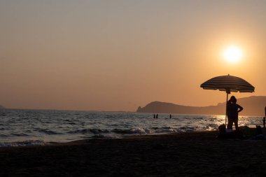 Güneş ışığında gün batımında yüzen insanların siluetleri, Sperlonga yakınlarındaki kumlu plajlar, Lazio, İtalya, yaz tatili