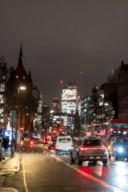 Londra sokakları geceleri araba farları ve ıslak yollardaki yansımalarla parıldıyor, canlı, atmosferik şehir manzarası yaratıyor, İngiltere
