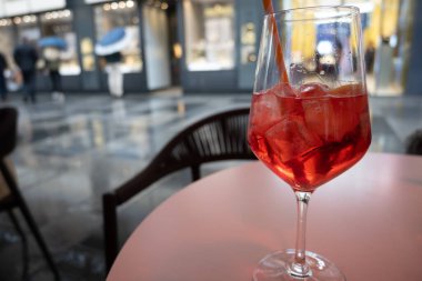 Bir bardak Aperol Spritz içeceği İtalya 'da yağmurda, küçük bir sokak kafesinde, yağmurlu bir sokakta ve dükkanların ışıklarında servis edilir.