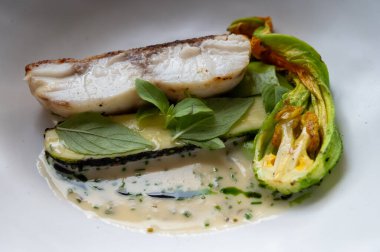 Fransız restoranında şefle güzel bir yemek, beyaz balıklı ana yemek, genç kabak kabakları, çiçekler, taze sürüler ve beyaz krema sosu.