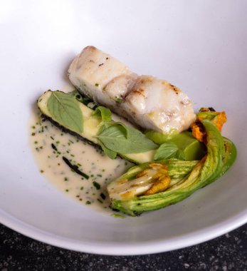 Fransız restoranında şefle güzel bir yemek, beyaz balıklı ana yemek, genç kabak kabakları, çiçekler, taze sürüler ve beyaz krema sosu.